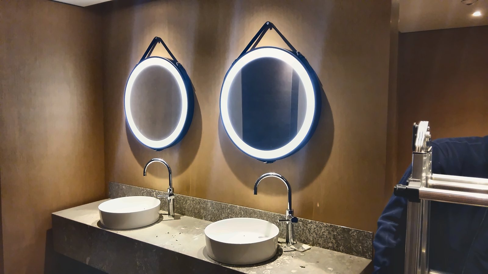 Deux miroirs circulaires rétroéclairés suspendus à des sangles au-dessus des lavabos de la salle de bains