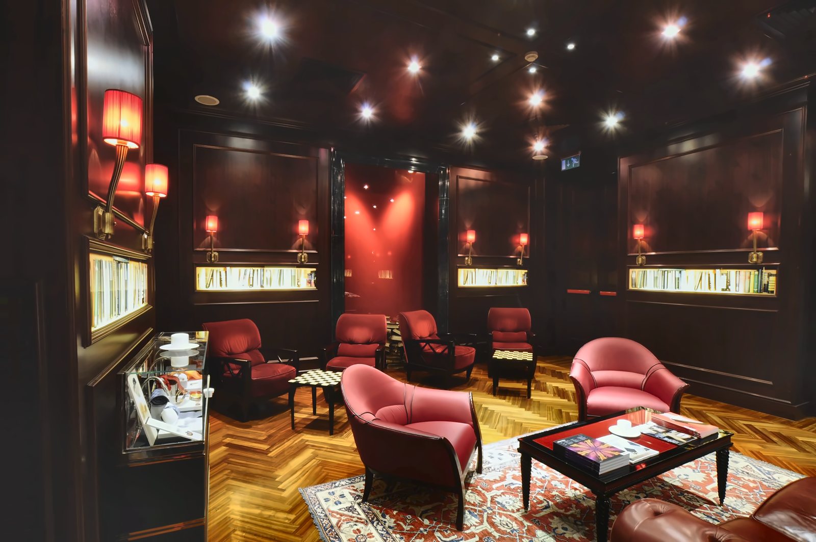 La lounge dell'Aleph con le poltrone rosse, le nicchie di libri e le applique a paralume plissettato rosso lungo le pareti in legno scuro