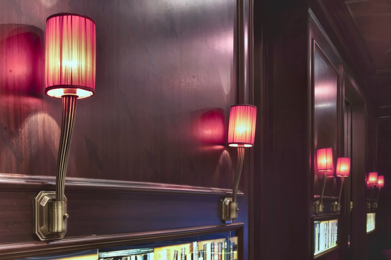 Le applique con paralume rosso riflesse nello specchio del corridoio, sopra le nicchie di libri