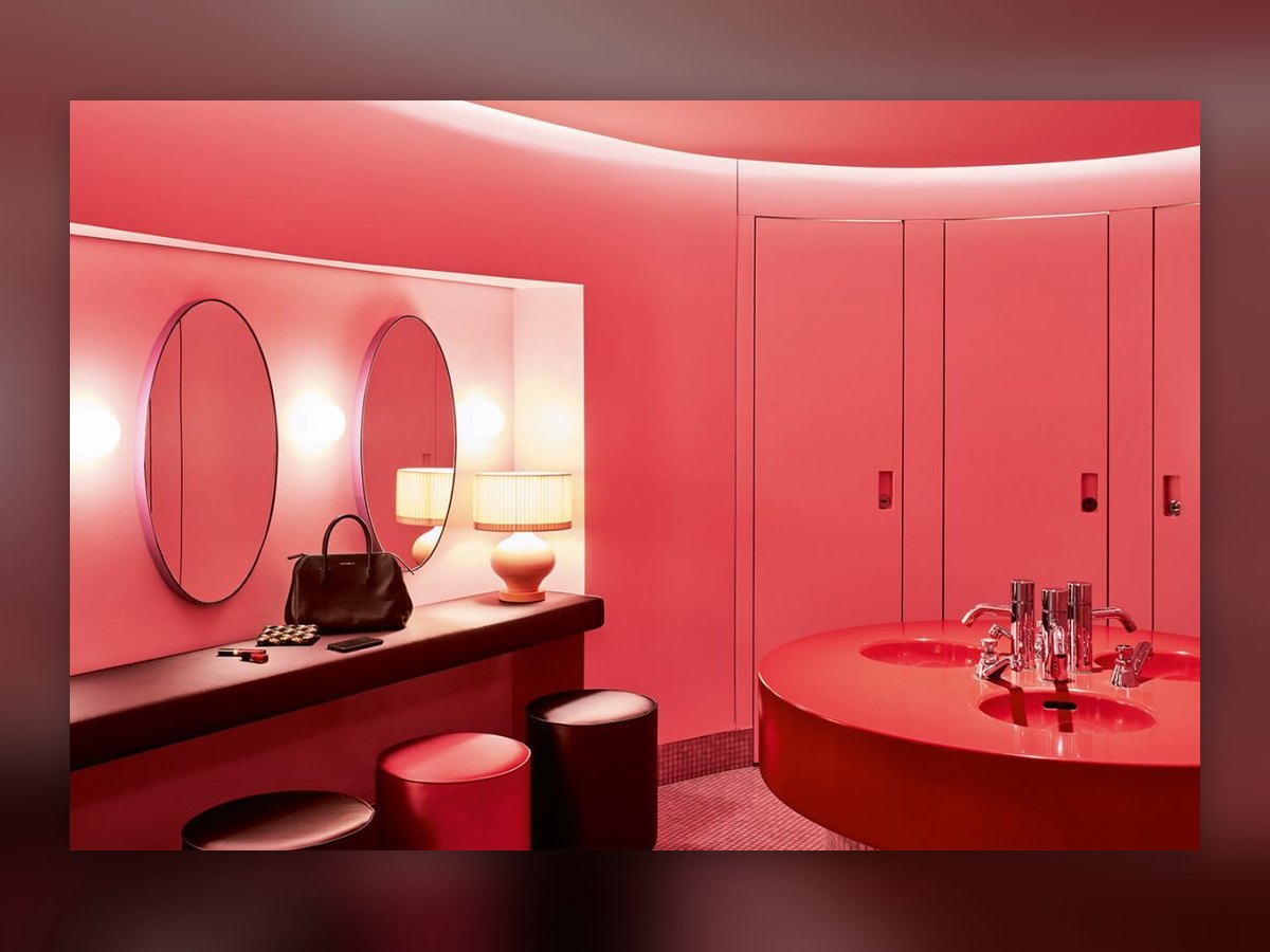 Due lampade da tavolo con paralume plissettato sul piano del bagno rosso, fra gli specchi ovali