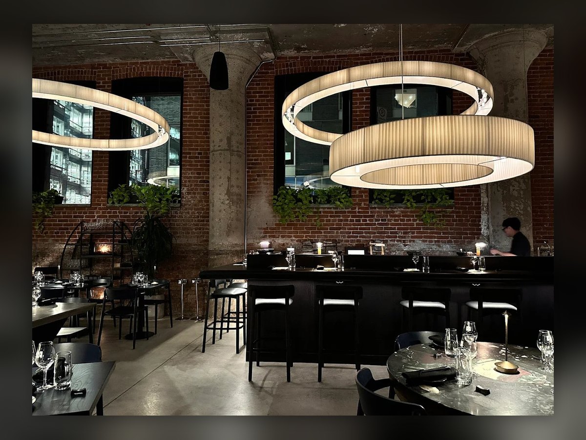 La sala del NAMA Omakase di Montreal: tre anelli plissettati sospesi sopra il banco, fra i pilastri e il muro di mattoni