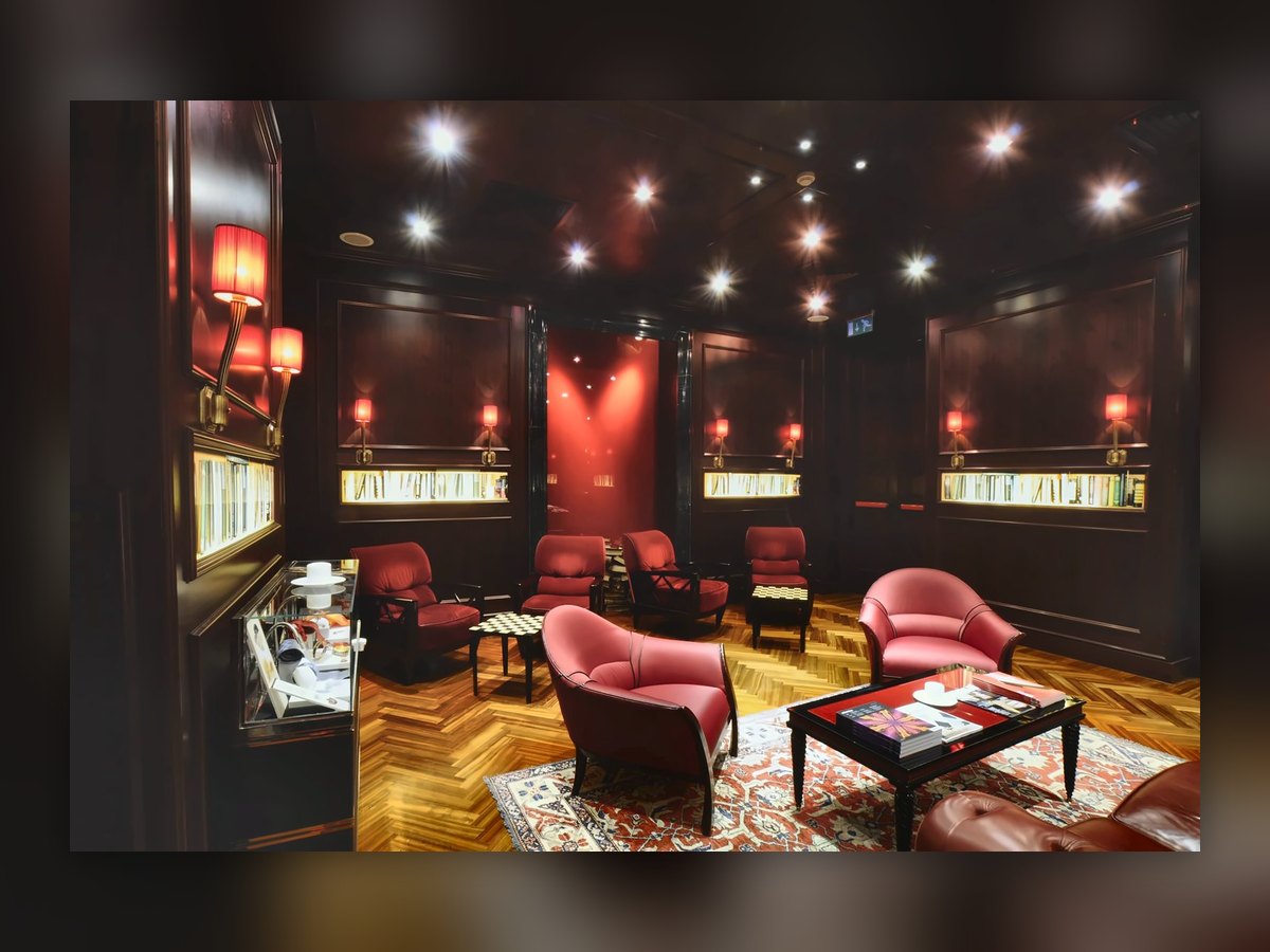 La lounge dell'Aleph con le poltrone rosse, le nicchie di libri e le applique a paralume plissettato rosso lungo le pareti in legno scuro