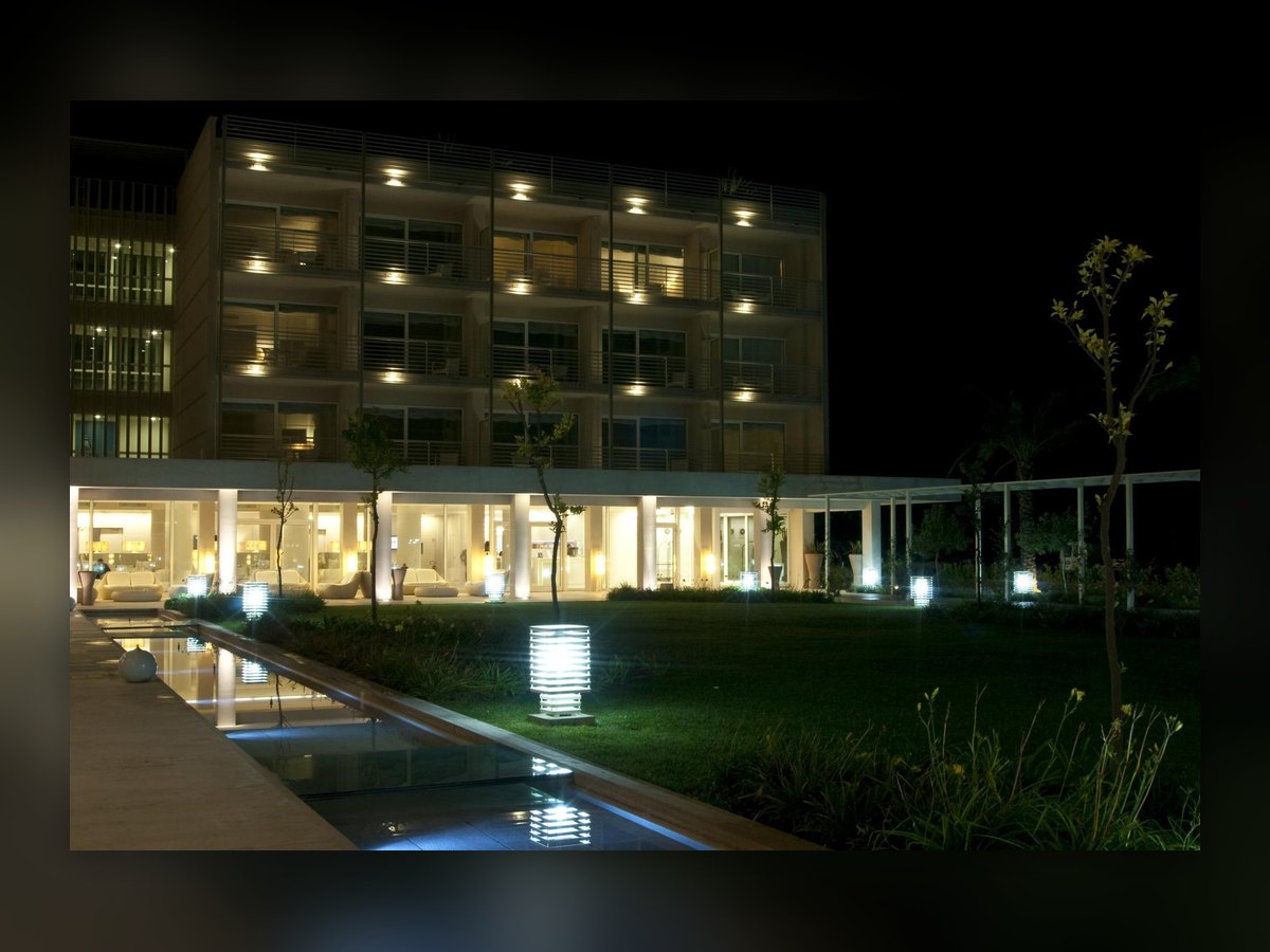La facciata dell'albergo di notte, con lo specchio d'acqua davanti e un paletto a lamelle acceso sul prato