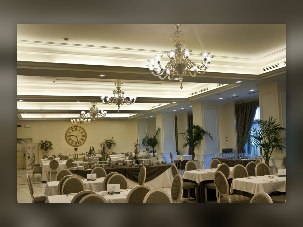 La sala banchetti apparecchiata, con i lampadari in vetro soffiato allineati sotto il soffitto a cassettoni