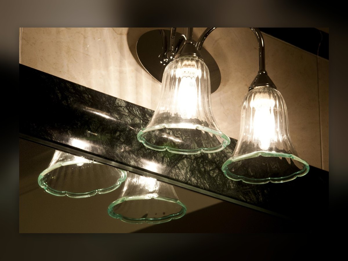 Two glass bells on curved arms, doubled by their reflection in the dark mirror below