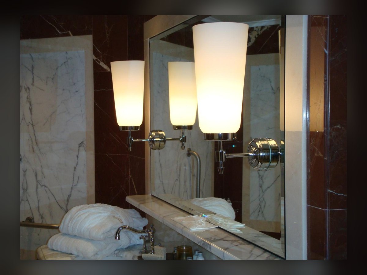 I cilindri in vetro opalino accesi sullo specchio del bagno, fra i marmi