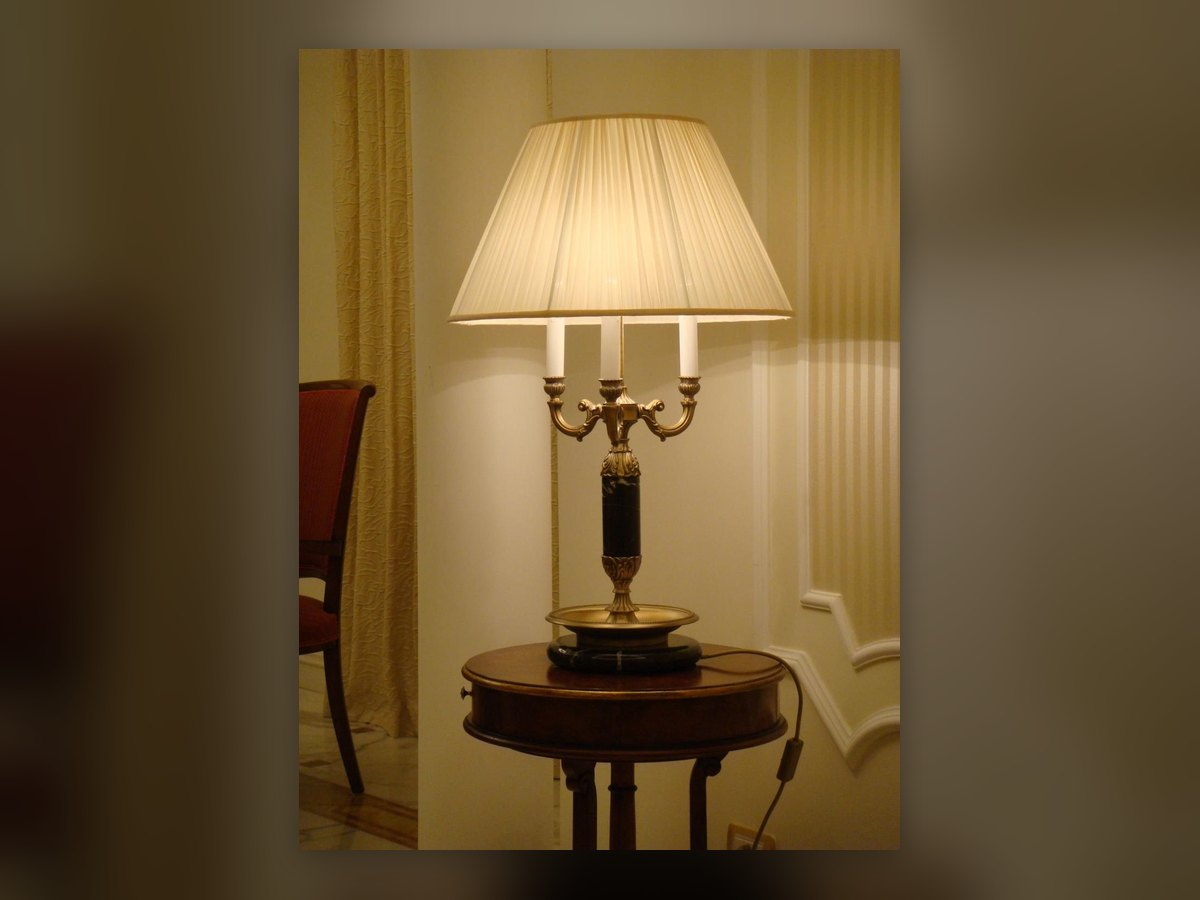 L'abat-jour con paralume plissettato su una base a candelabro in bronzo, sul tavolino tondo