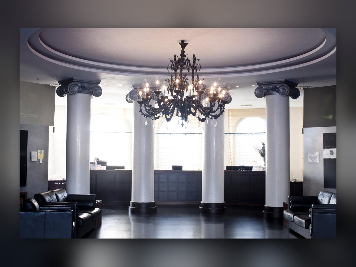 Il lampadario in vetro nero sospeso fra le colonne bianche della hall, sopra il pavimento scuro