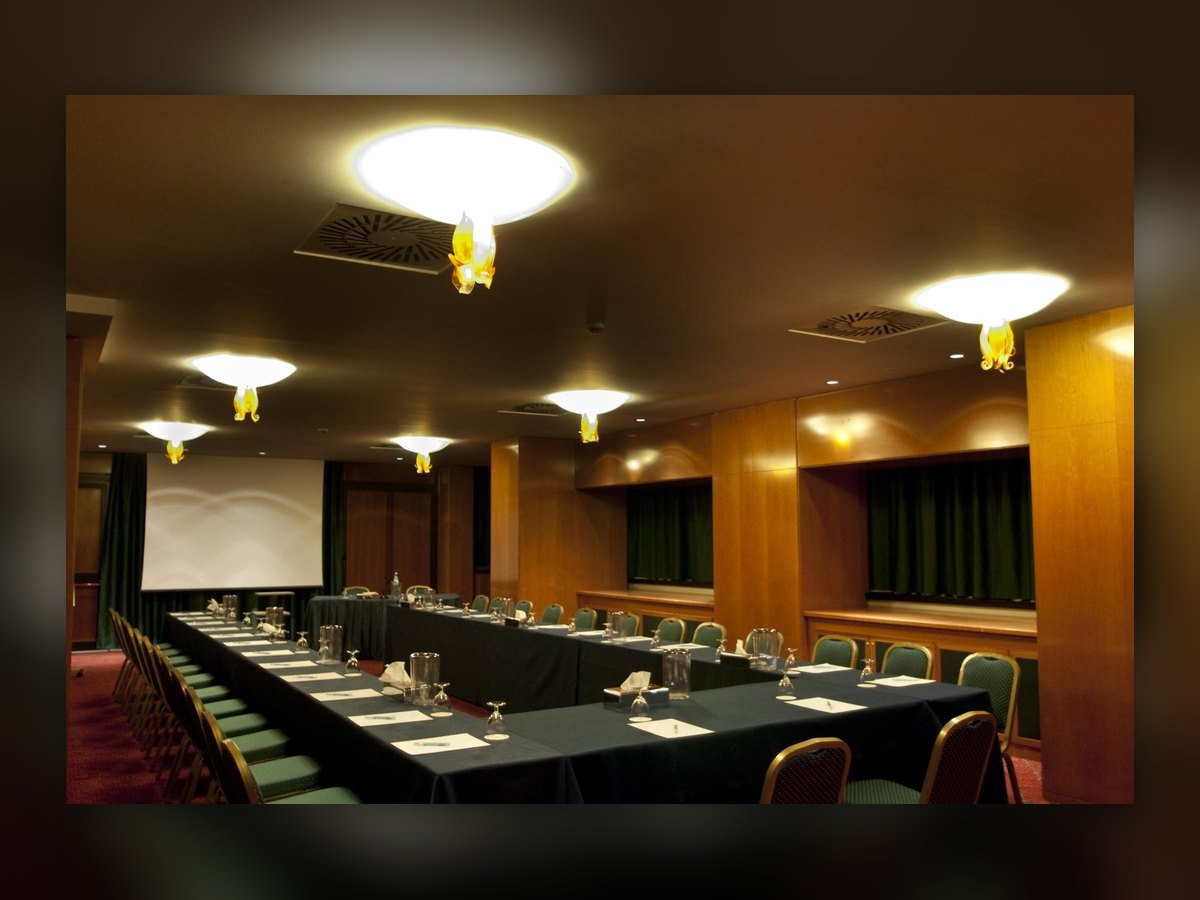 La sala riunioni con il tavolo apparecchiato e le coppe opaline accese a soffitto