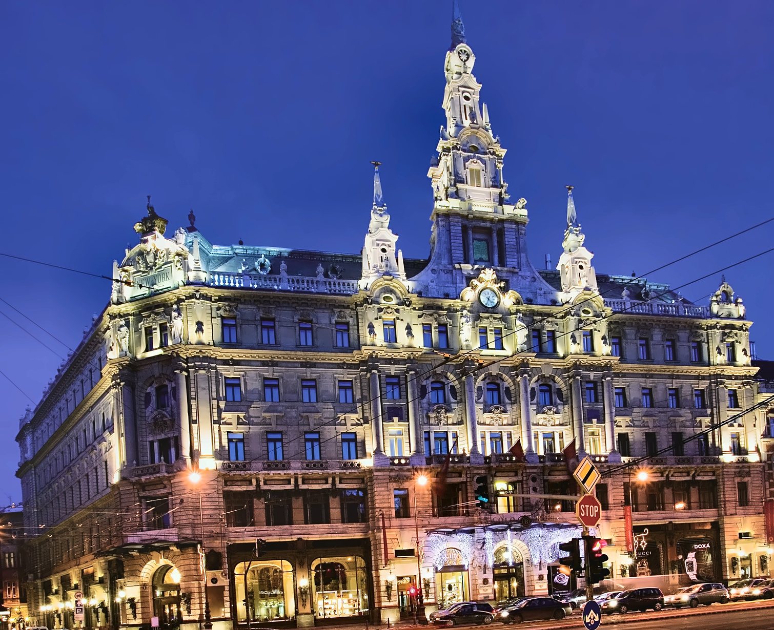 Der beleuchtete New York Palace in Budapest unter tiefblauem Himmel: der Mittelturm, die Uhr und der Schriftzug New York auf dem Eckgiebel