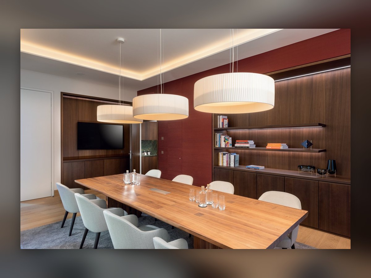 The presidential suite of the Mövenpick Hotel Basel: three pleated drum pendants above the long wooden table, a dark red wall and lit shelves