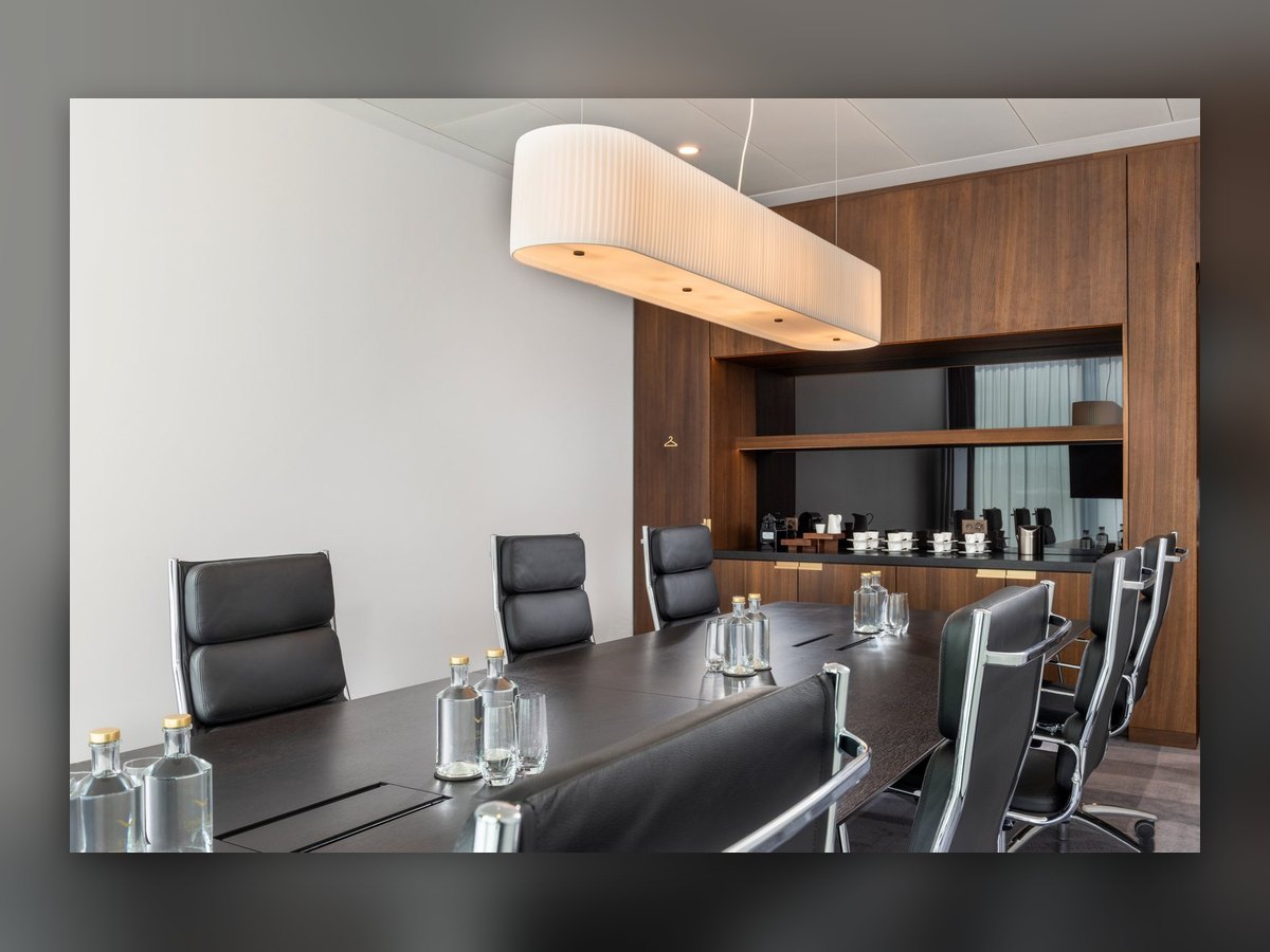 A meeting room at the Mövenpick Hotel Basel: an elongated oval pendant with a pleated band above the dark table and black leather chairs